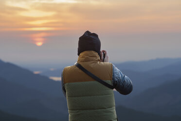 Rückansicht eines männlichen Wanderers, der bei Sonnenuntergang die Berge fotografiert - CAVF30131