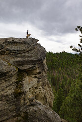 Low angle view of man and dog standing on cliff against cloudy sky - CAVF30146