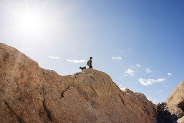 Low angle view of man with dog standing on mountain against blue sky - CAVF30154