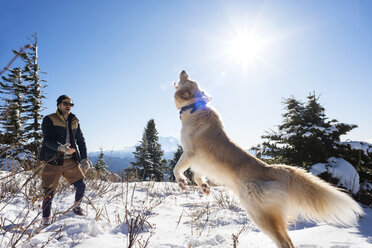 Mann spielt mit Hund auf schneebedecktem Berg gegen Himmel - CAVF30181
