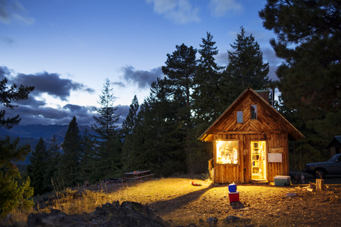 Beleuchtete Holzhütte im Wald bei Nacht, lizenzfreies Stockfoto