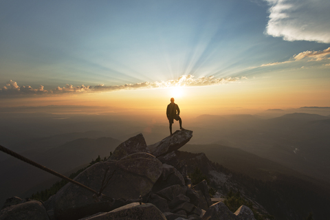 Mann steht auf einem Felsen an einer Klippe gegen den Himmel bei Sonnenuntergang, lizenzfreies Stockfoto