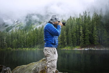 Side view of man photographing while standing against lake - CAVF30252