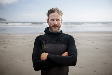 Porträt eines reifen Surfers, der mit verschränkten Armen am Strand steht - CAVF30260