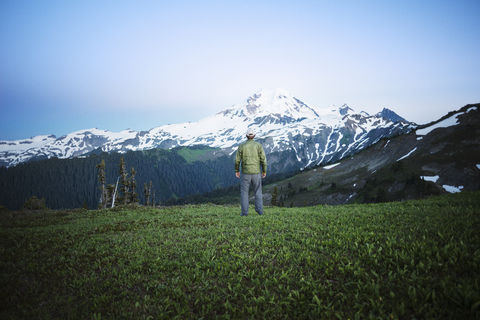 Rückansicht eines Mannes, der auf einem grasbewachsenen Feld vor einem Berg steht, lizenzfreies Stockfoto