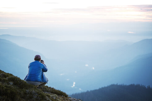 Rückansicht eines Mannes, der auf einem Berg kauernd gegen den Himmel fotografiert - CAVF30288