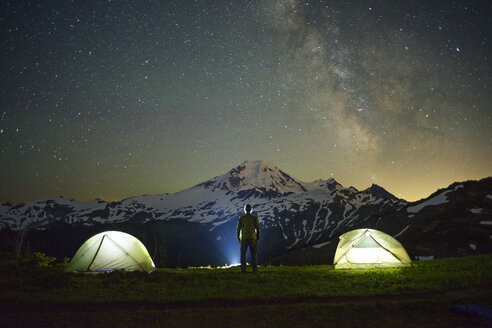 Rückansicht eines Mannes, der auf einem Feld bei Zelten vor einem Sternenhimmel steht - CAVF30292