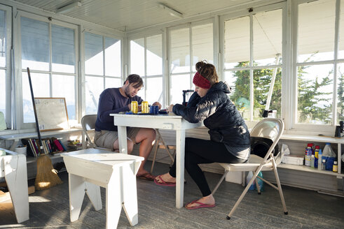 Ein Paar liest ein Buch, während es am Tisch in einer Hütte sitzt - CAVF30321