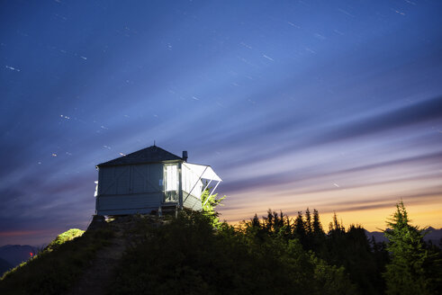 Beleuchtete Hütte auf einem Berg gegen bewölkten Himmel bei Nacht - CAVF30324