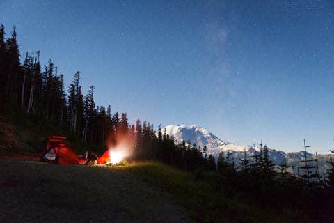 Beleuchtetes Zelt auf einem Hügel am Waldrand gegen den nächtlichen Himmel, lizenzfreies Stockfoto