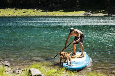 Mann und Hund auf Paddelbrett am Seeufer - CAVF30328