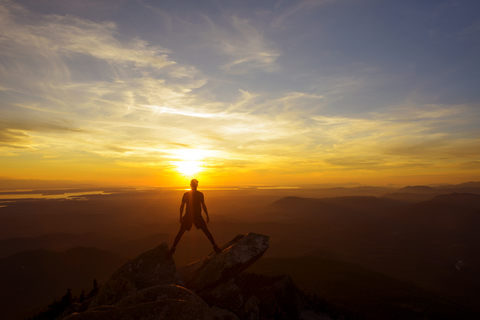 Wanderer in voller Länge auf dem Gipfel eines Berges stehend gegen den Himmel bei Sonnenuntergang, lizenzfreies Stockfoto