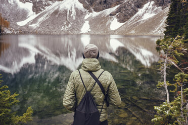 Rückansicht eines Mannes mit Rucksack, der im Winter am Seeufer steht - CAVF30339