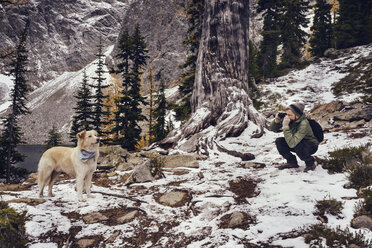 Mann fotografiert Hund im Winter im Wald - CAVF30340