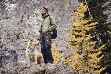 Niedriger Blickwinkel auf einen Mann mit Hund, der im Winter auf einer Felsformation steht - CAVF30341