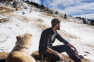 Mann mit Hund entspannt sich im Winter auf einem Feld - CAVF30351