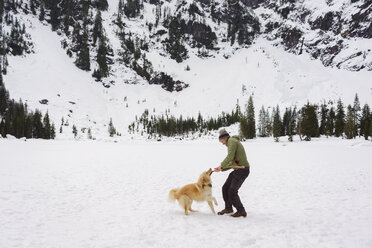 Glücklicher Mann spielt mit Golden Retriever auf schneebedecktem Feld - CAVF30363