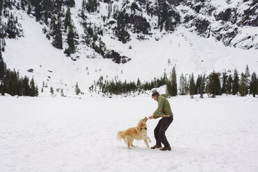 Happy man playing with Golden Retriever on snow covered field - CAVF30363