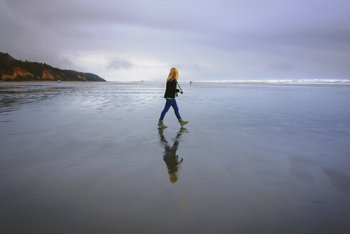 Seitenansicht einer Frau mit Kamera, die am Strand gegen den bewölkten Himmel läuft - CAVF30368