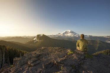 Rear view of male hiker sitting on mountain against clear sky - CAVF30378