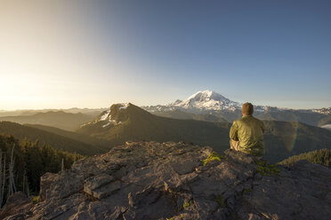 Rückansicht eines männlichen Wanderers auf einem Berg sitzend gegen den klaren Himmel - CAVF30378