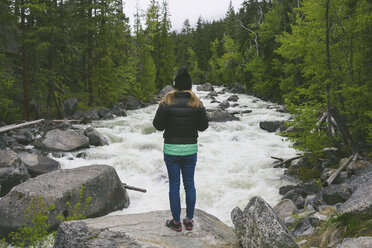 Rear view of hiker standing on rock over river at forest - CAVF30390