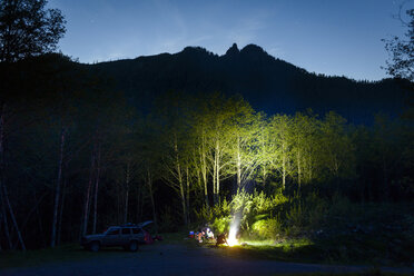Wanderer kampieren am Lagerfeuer in der Abenddämmerung vor den Bergen - CAVF30392