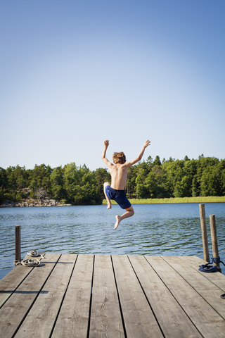 Rückansicht eines Jungen, der vom Steg ins Wasser springt, lizenzfreies Stockfoto