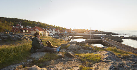 Ältere Frau mit Hund sitzt an der Küste von Bornholm, Dänemark - FOLF02375