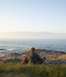 Mature woman with dogs sitting on rocky coastline at Bornholm, Denmark - FOLF02376