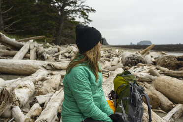 Nachdenkliche Wanderin schaut weg, während sie auf einem Baumstamm an der Olympic Coast sitzt - CAVF30398