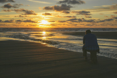 Rückansicht eines knienden Wanderers am Long Beach bei Sonnenuntergang - CAVF30399