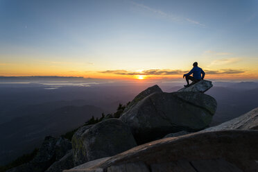 Man sitting on rock against sky at Mount Pilchuck State Park during sunset - CAVF30406