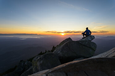 Mann sitzt auf einem Felsen gegen den Himmel im Mount Pilchuck State Park bei Sonnenuntergang - CAVF30406