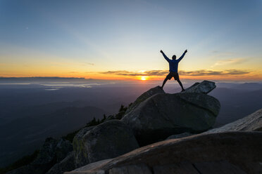 Silhouette man with arms raised standing on rocks against sky at Mount Pilchuck State Park during sunset - CAVF30407