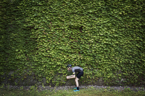 Side view of man bending against ivy covered building - CAVF30435