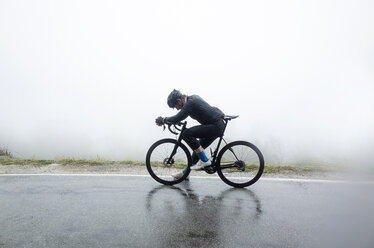 Mann entspannt sich auf dem Fahrrad auf nasser Straße bei nebligem Wetter - CAVF30486