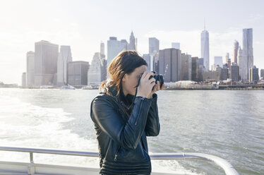 Seitenansicht einer Frau, die auf einem Boot stehend vor einer Stadtkulisse fotografiert - CAVF30491