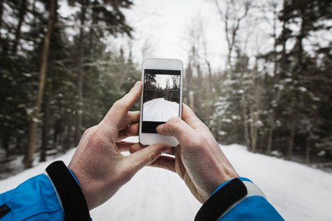 Ausgeschnittenes Bild einer Hand, die mit einem Mobiltelefon einen verschneiten Weg fotografiert, lizenzfreies Stockfoto