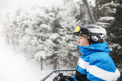 Seitenansicht eines Mannes im Skilift vor schneebedeckten Bäumen, lizenzfreies Stockfoto