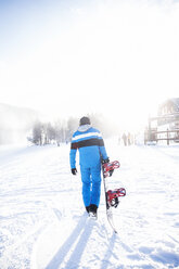 Rückansicht eines Mannes mit Snowboard auf einem schneebedeckten Feld - CAVF30538