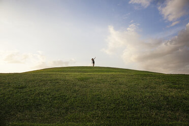 Distant view of woman standing on grassy field against sky - CAVF30561