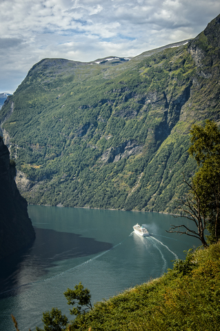 Ship sailing by mountains in Geirangerfjord stock photo