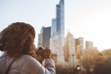 Rear view of woman photographing skyscrapers through digital camera against clear sky - CAVF30576