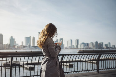 Seitenansicht einer Frau, die ihr Smartphone auf dem Fußweg am Hafen benutzt - CAVF30579