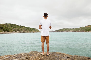 Rear view of young man standing at lakeshore - CAVF30610