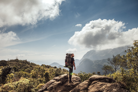 Seitenansicht eines männlichen Rucksacktouristen, der auf einem Berg vor einem bewölkten Himmel steht, lizenzfreies Stockfoto