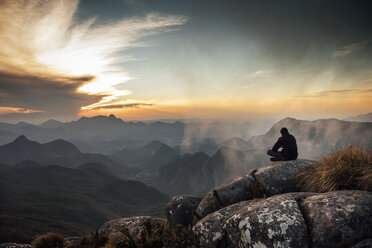 Rückansicht eines auf einem Berg sitzenden Mannes bei Sonnenuntergang - CAVF30618
