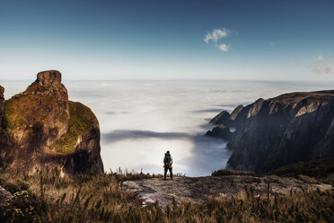 Rear view of male hiker standing on mountain against sky - CAVF30625