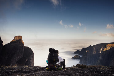 Rear view of backpacker sitting on mountain against sky - CAVF30626